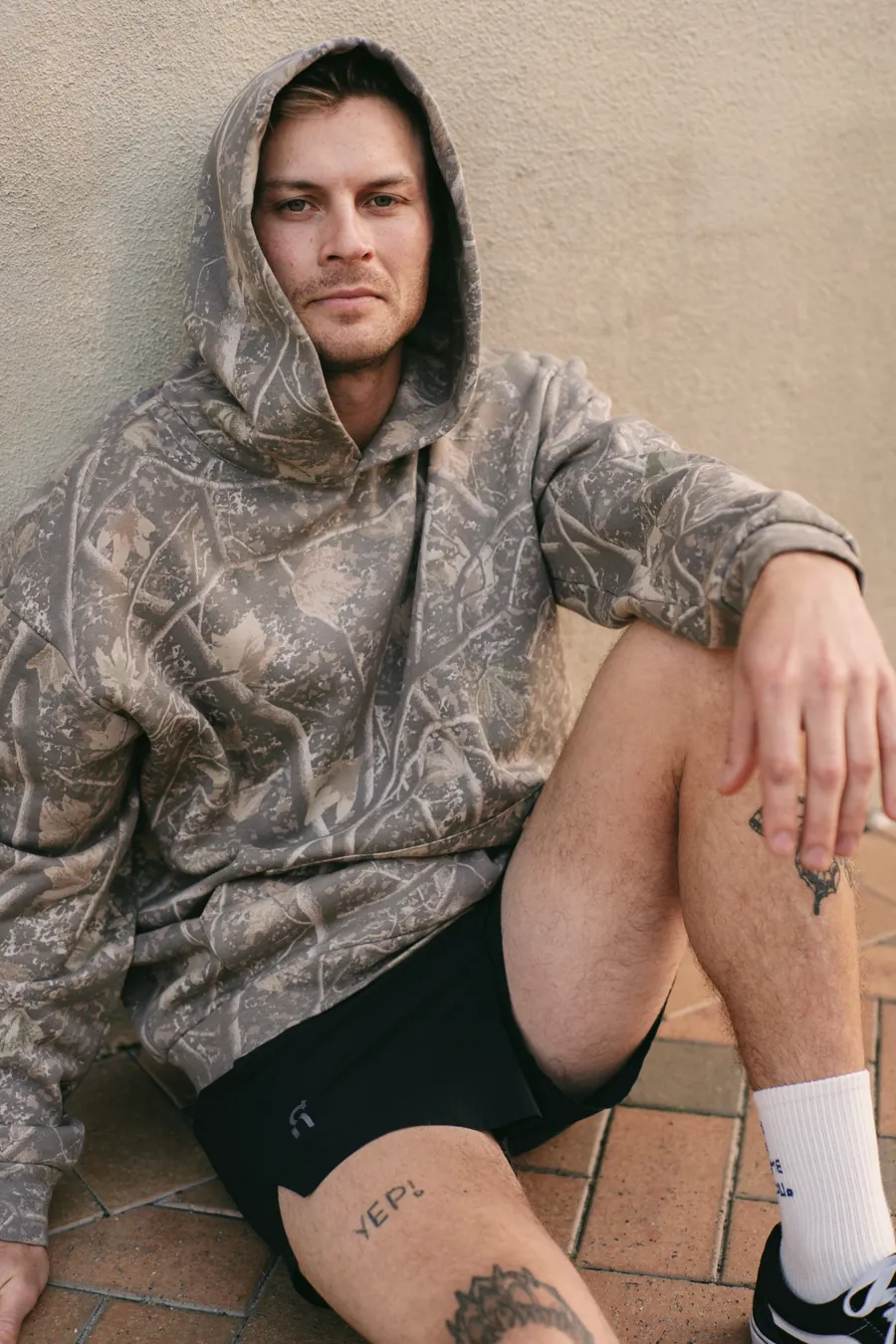 Man kneeling in a Deadwood Camo Heavyweight hoodie